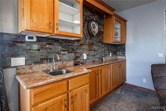 kitchen featuring a sink, baseboards, light stone countertops, tasteful backsplash, and glass insert cabinets