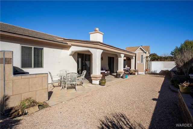 back of property featuring outdoor dining space, a chimney, fence, a patio area, and stucco siding