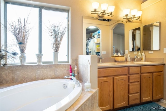 full bathroom with double vanity, an inviting chandelier, a garden tub, and a sink