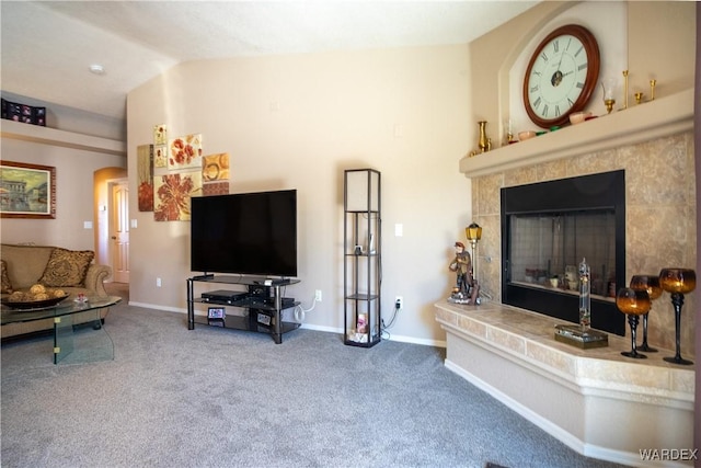 living room with baseboards, arched walkways, a tiled fireplace, vaulted ceiling, and carpet floors