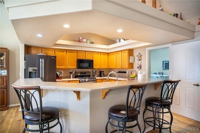 kitchen featuring stainless steel appliances, light wood-type flooring, a raised ceiling, and light countertops