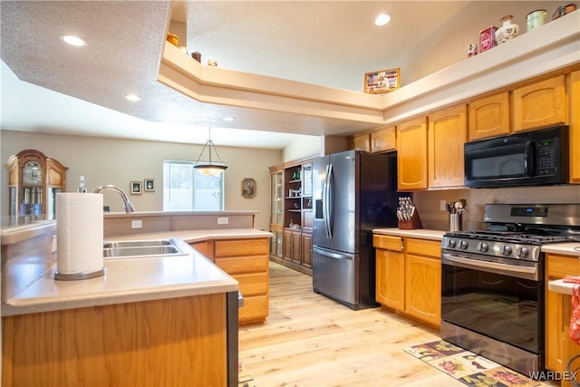 kitchen with light wood finished floors, a raised ceiling, light countertops, stainless steel appliances, and a sink