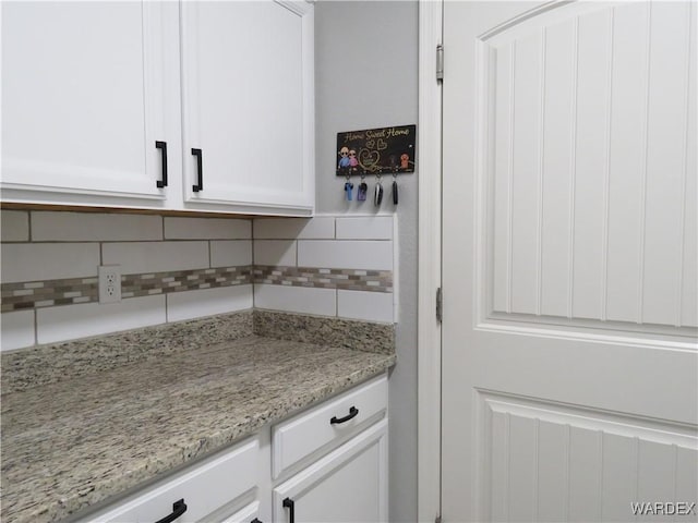 interior space with tasteful backsplash, light stone counters, and white cabinets