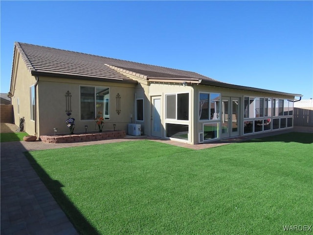 rear view of house with a yard, ac unit, a sunroom, and stucco siding