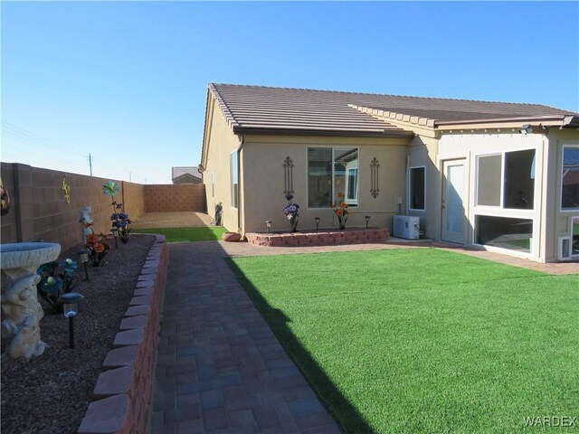 back of property featuring a yard, central AC unit, a fenced backyard, and stucco siding