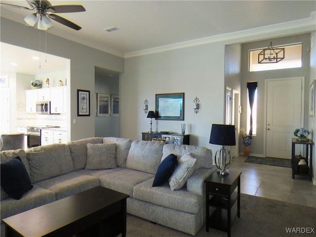 living room with ceiling fan, visible vents, crown molding, and dark tile patterned flooring