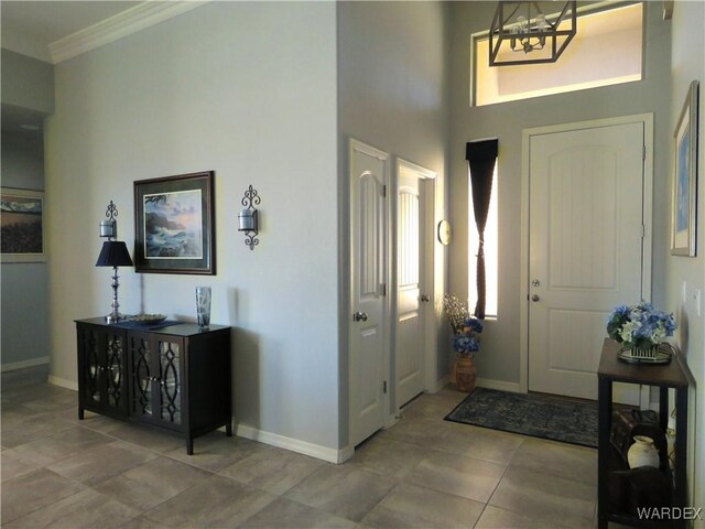 tiled foyer featuring baseboards, a notable chandelier, and crown molding