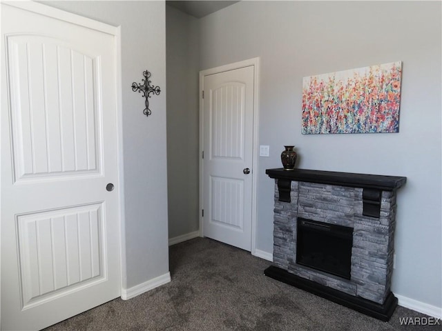 unfurnished living room featuring dark carpet, a stone fireplace, and baseboards