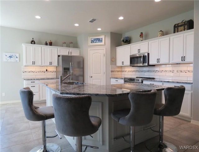 kitchen featuring a breakfast bar area, stainless steel appliances, visible vents, white cabinetry, and an island with sink