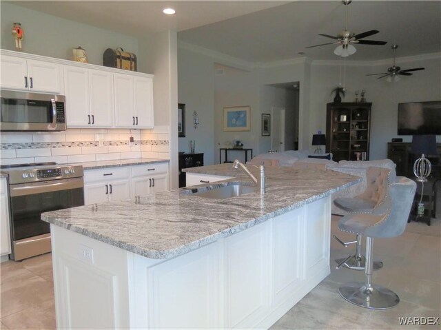 kitchen featuring stainless steel appliances, a sink, white cabinetry, backsplash, and an island with sink