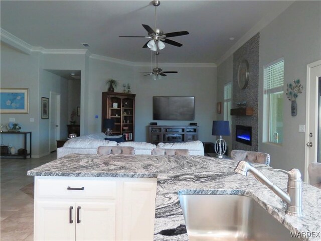 kitchen with a sink, white cabinetry, open floor plan, light stone countertops, and crown molding