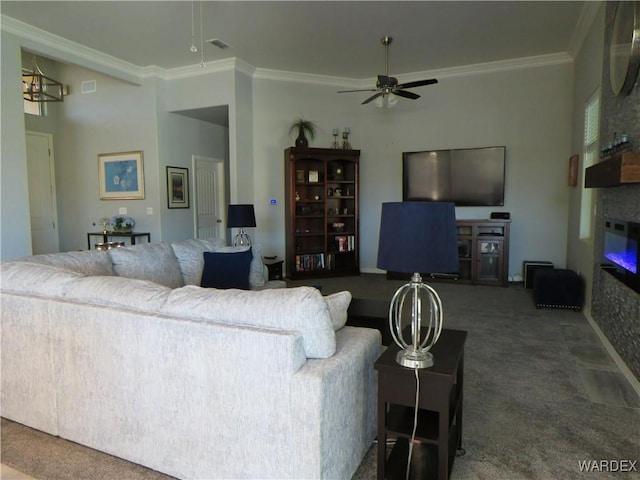 carpeted living room with a large fireplace, visible vents, a ceiling fan, and crown molding