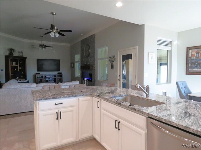 kitchen featuring light stone counters, stainless steel dishwasher, open floor plan, white cabinets, and a sink