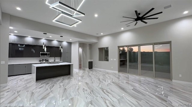 kitchen with decorative light fixtures, a center island with sink, light countertops, appliances with stainless steel finishes, and modern cabinets