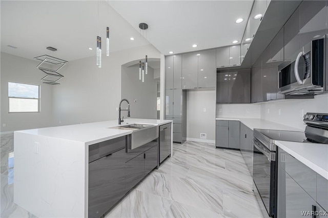 kitchen featuring an island with sink, modern cabinets, appliances with stainless steel finishes, decorative light fixtures, and gray cabinets