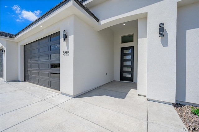 property entrance featuring concrete driveway, an attached garage, and stucco siding