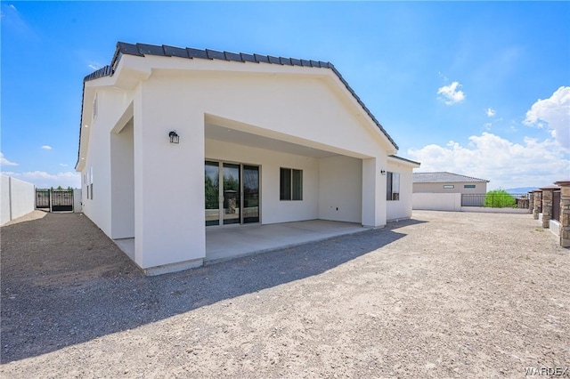 rear view of property featuring a patio area, fence, and stucco siding