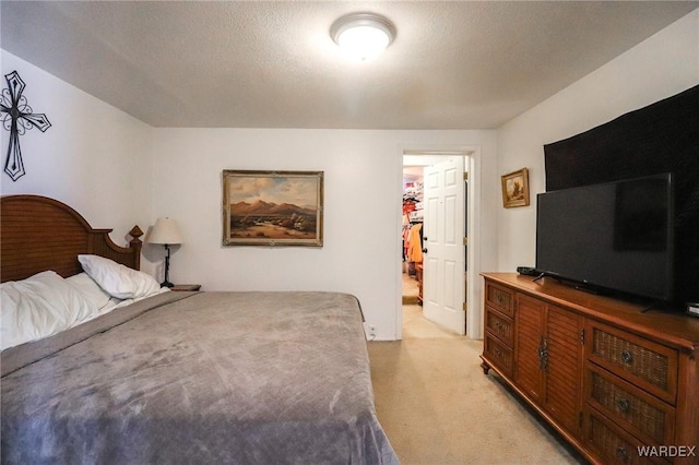 bedroom featuring light carpet, a walk in closet, and a textured ceiling