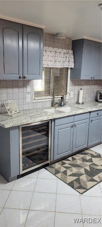 kitchen with light tile patterned floors, wine cooler, gray cabinetry, a sink, and tasteful backsplash