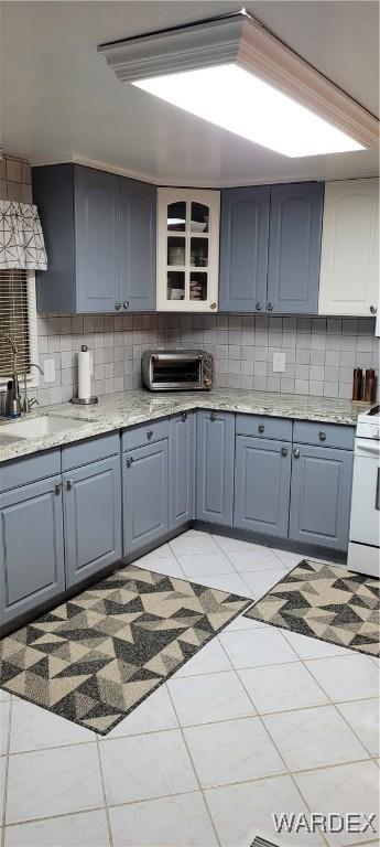 kitchen featuring light tile patterned floors, tasteful backsplash, a toaster, gas range gas stove, and a sink