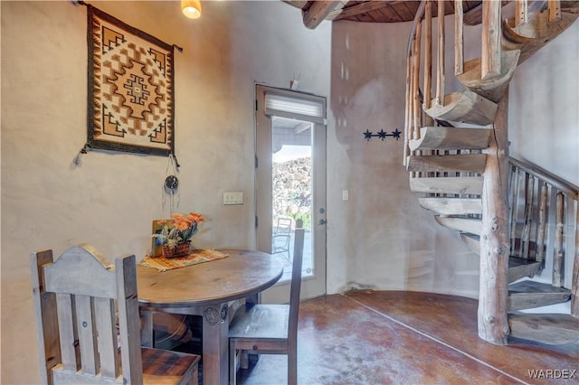 dining space featuring beamed ceiling, concrete floors, and stairs