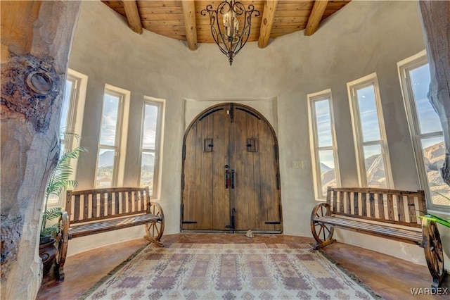 entrance foyer with beamed ceiling, wood ceiling, an inviting chandelier, a towering ceiling, and arched walkways