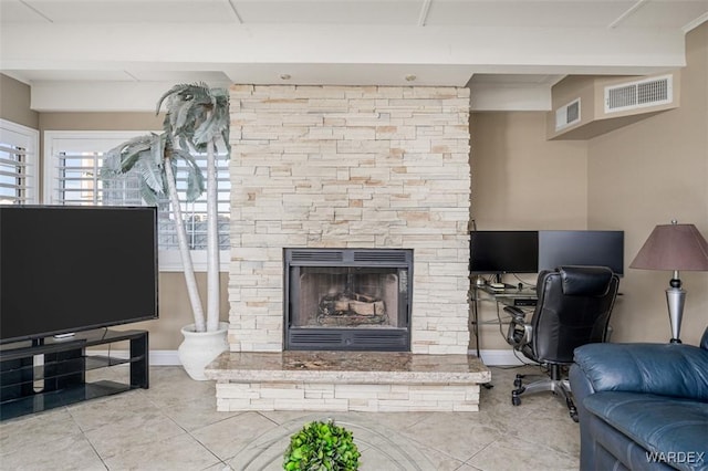 living area with a stone fireplace, visible vents, and baseboards