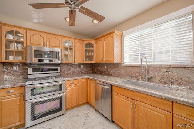 kitchen with decorative backsplash, glass insert cabinets, appliances with stainless steel finishes, light stone counters, and a sink