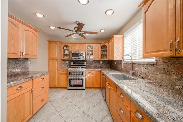 kitchen featuring glass insert cabinets, stone countertops, appliances with stainless steel finishes, and a sink