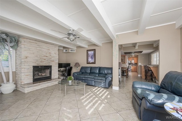 living area featuring ceiling fan, a stone fireplace, beam ceiling, and light tile patterned flooring