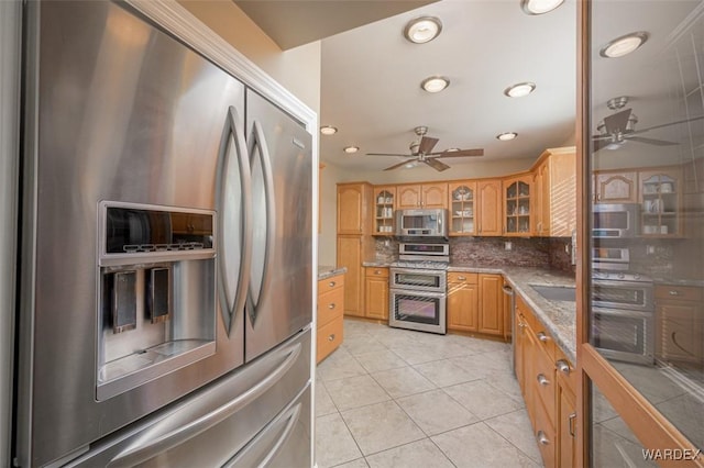 kitchen with light tile patterned floors, stainless steel appliances, a ceiling fan, decorative backsplash, and glass insert cabinets