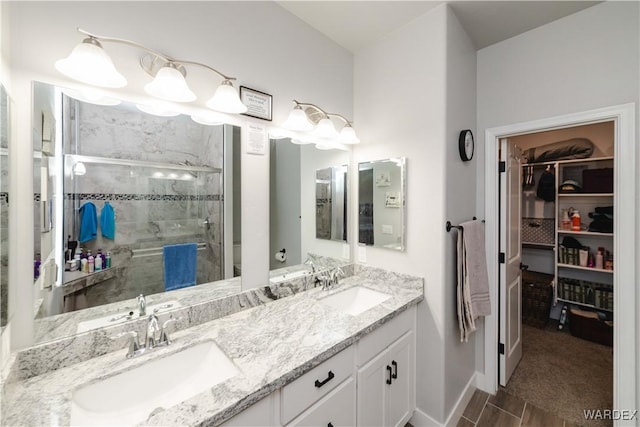 bathroom with a sink, a spacious closet, double vanity, and a stall shower