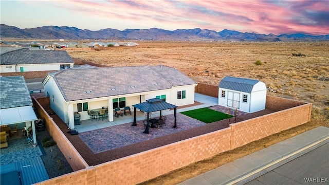exterior space with a mountain view, a storage shed, a gazebo, a fenced backyard, and an outbuilding