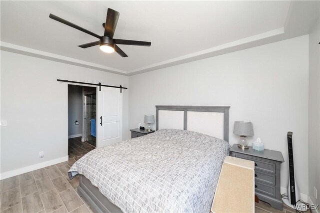 bedroom with a barn door, baseboards, ceiling fan, and wood finish floors