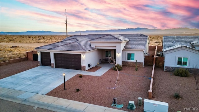 view of front of house featuring stucco siding, a mountain view, stone siding, an attached garage, and a tiled roof