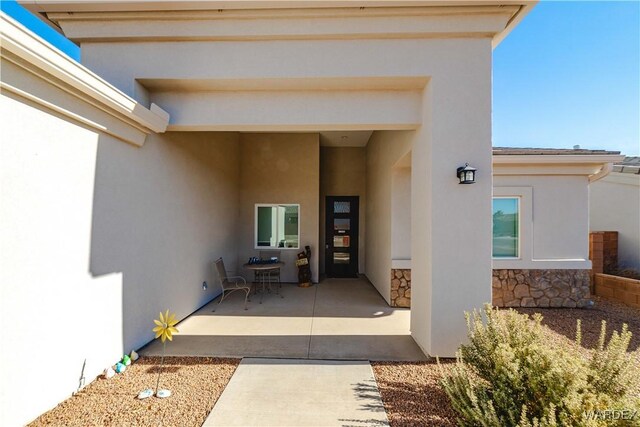 view of exterior entry with stone siding, a patio, and stucco siding