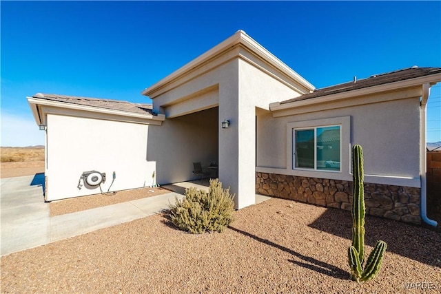 doorway to property featuring a patio, stucco siding, and stone siding