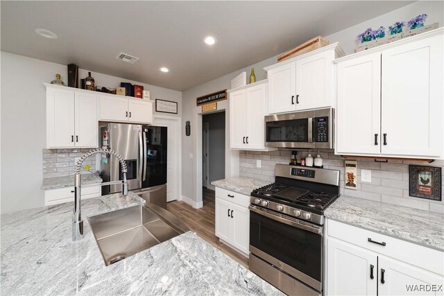 kitchen featuring stainless steel appliances, white cabinets, a sink, and visible vents