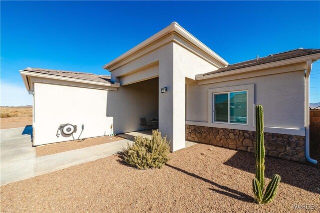 rear view of property featuring stone siding, driveway, an attached garage, and stucco siding