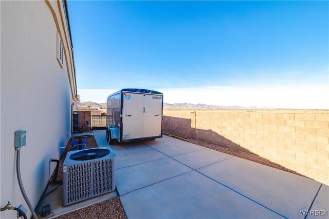 view of patio with central AC unit, a fenced backyard, an outbuilding, a storage unit, and a mountain view