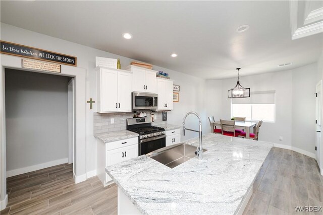 kitchen featuring a sink, white cabinetry, appliances with stainless steel finishes, light stone countertops, and an island with sink