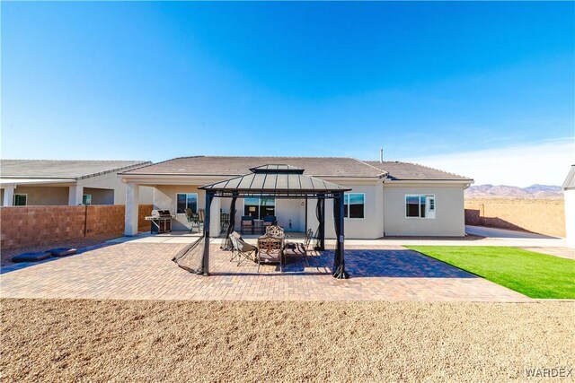 rear view of property featuring stucco siding, a gazebo, a patio area, a mountain view, and fence