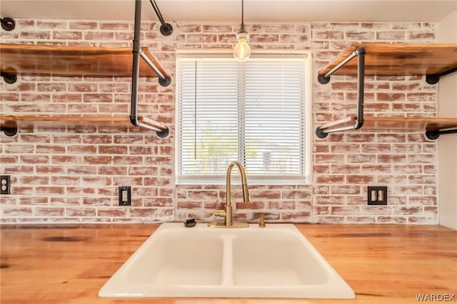 kitchen with butcher block countertops, a sink, and brick wall