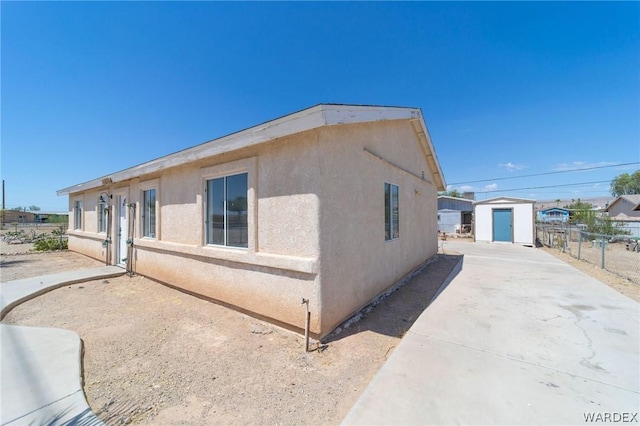 view of side of home featuring a storage shed, fence, stucco siding, and an outdoor structure