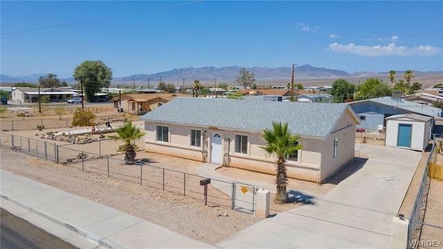 ranch-style home featuring a fenced front yard, a mountain view, a shingled roof, stucco siding, and a shed