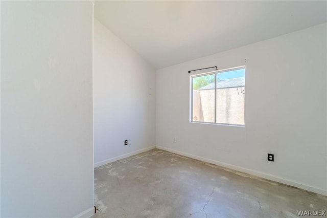 empty room featuring vaulted ceiling, concrete floors, and baseboards