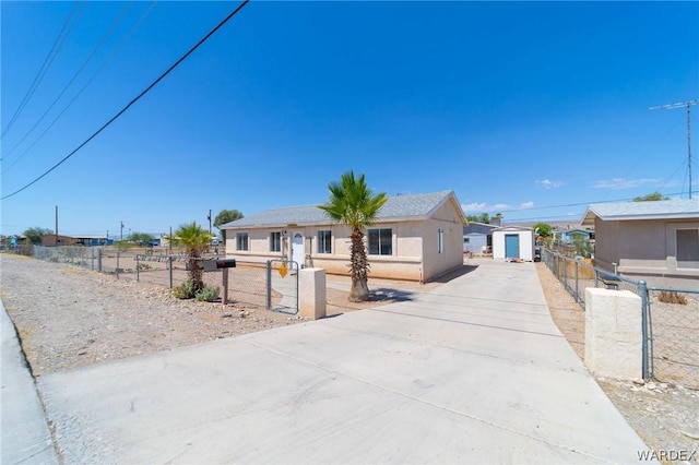 view of front of home with an outbuilding, a fenced front yard, concrete driveway, stucco siding, and a shed