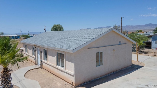 back of house with a shingled roof, a mountain view, and stucco siding