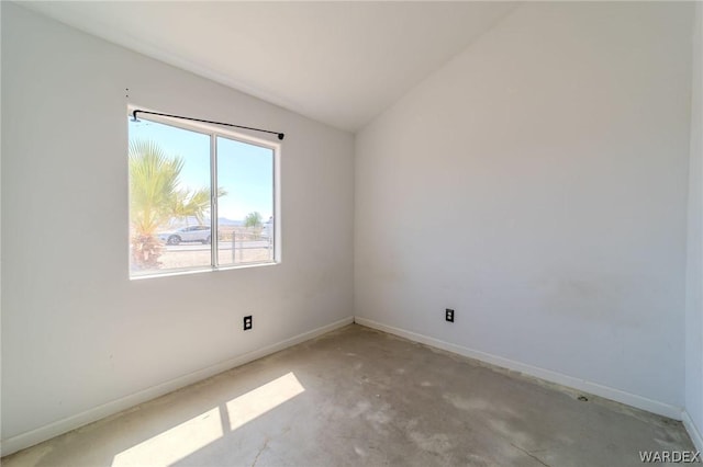 unfurnished room with lofted ceiling, concrete floors, and baseboards