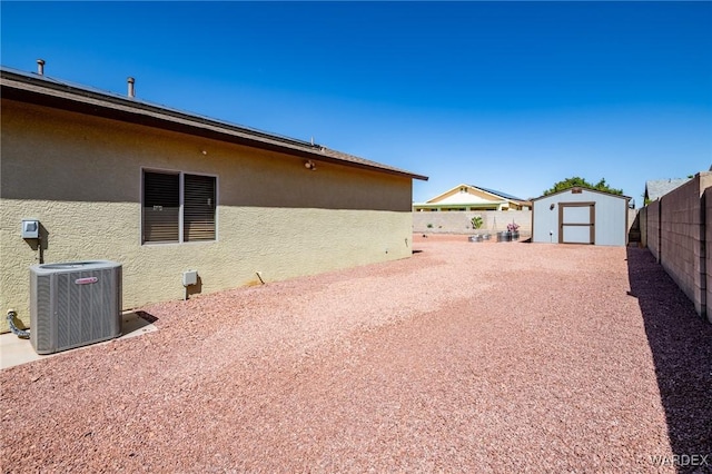 view of yard with central AC, a fenced backyard, an outbuilding, and a storage shed